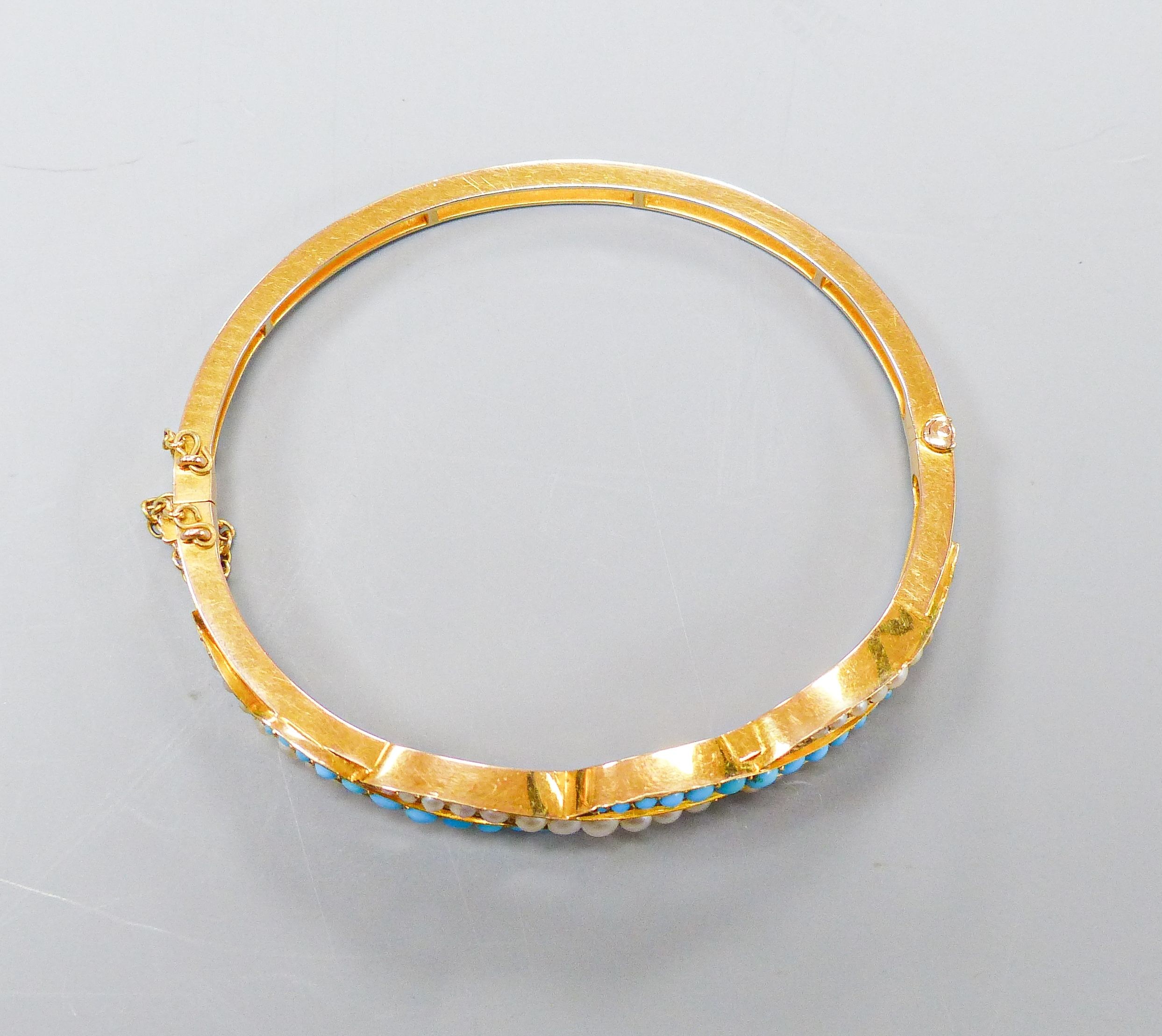 A boxed Edwardian yellow metal, graduated turquoise and seed pearl set hinged bangle, interior diameter 55mm, gross weight 15.5 grams.